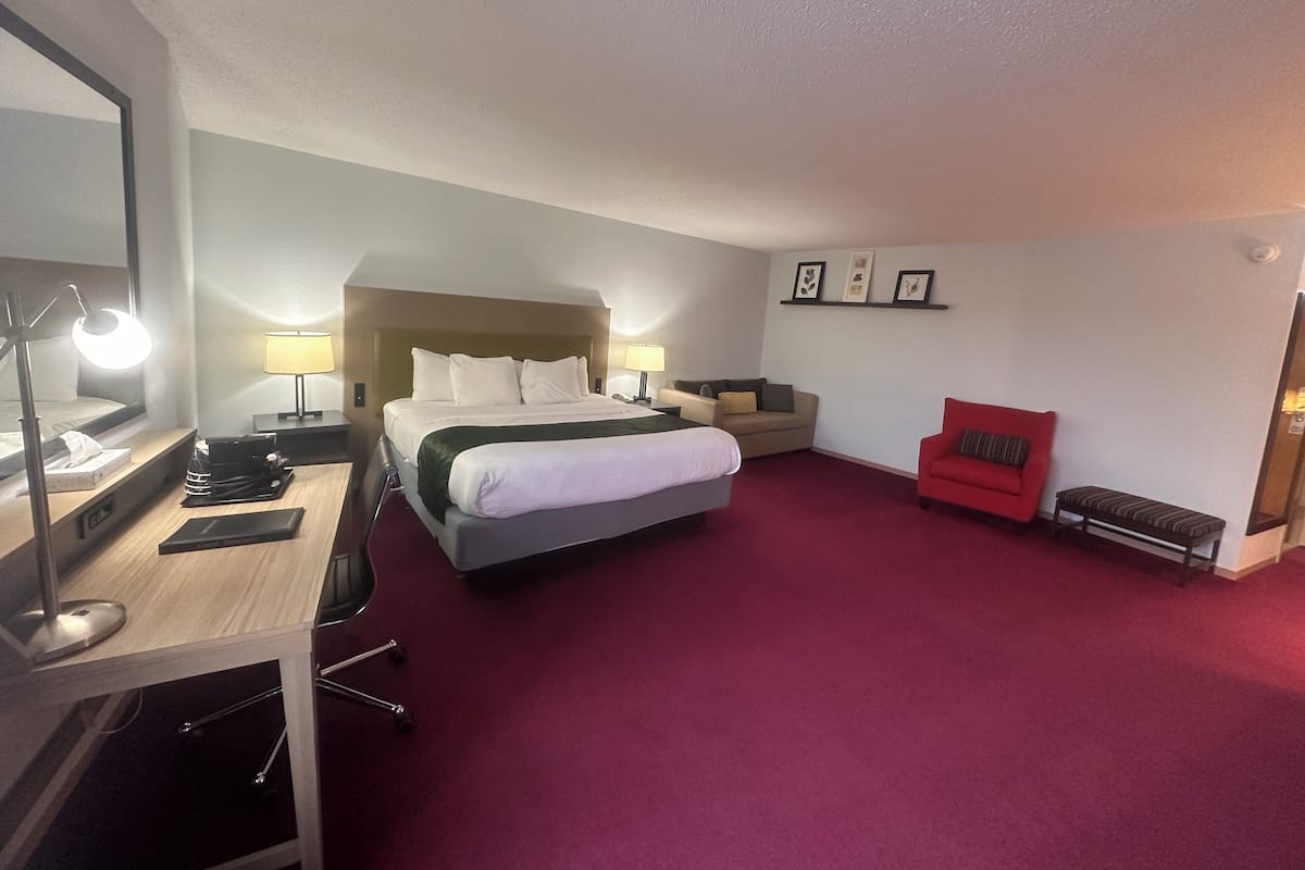 A hotel room with a bed, desk, chair, and a red sofa.