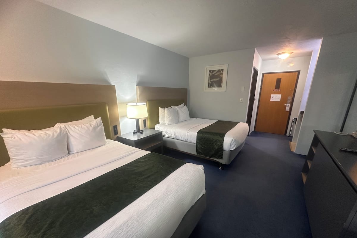 A hotel room with two beds, a desk, and a door.