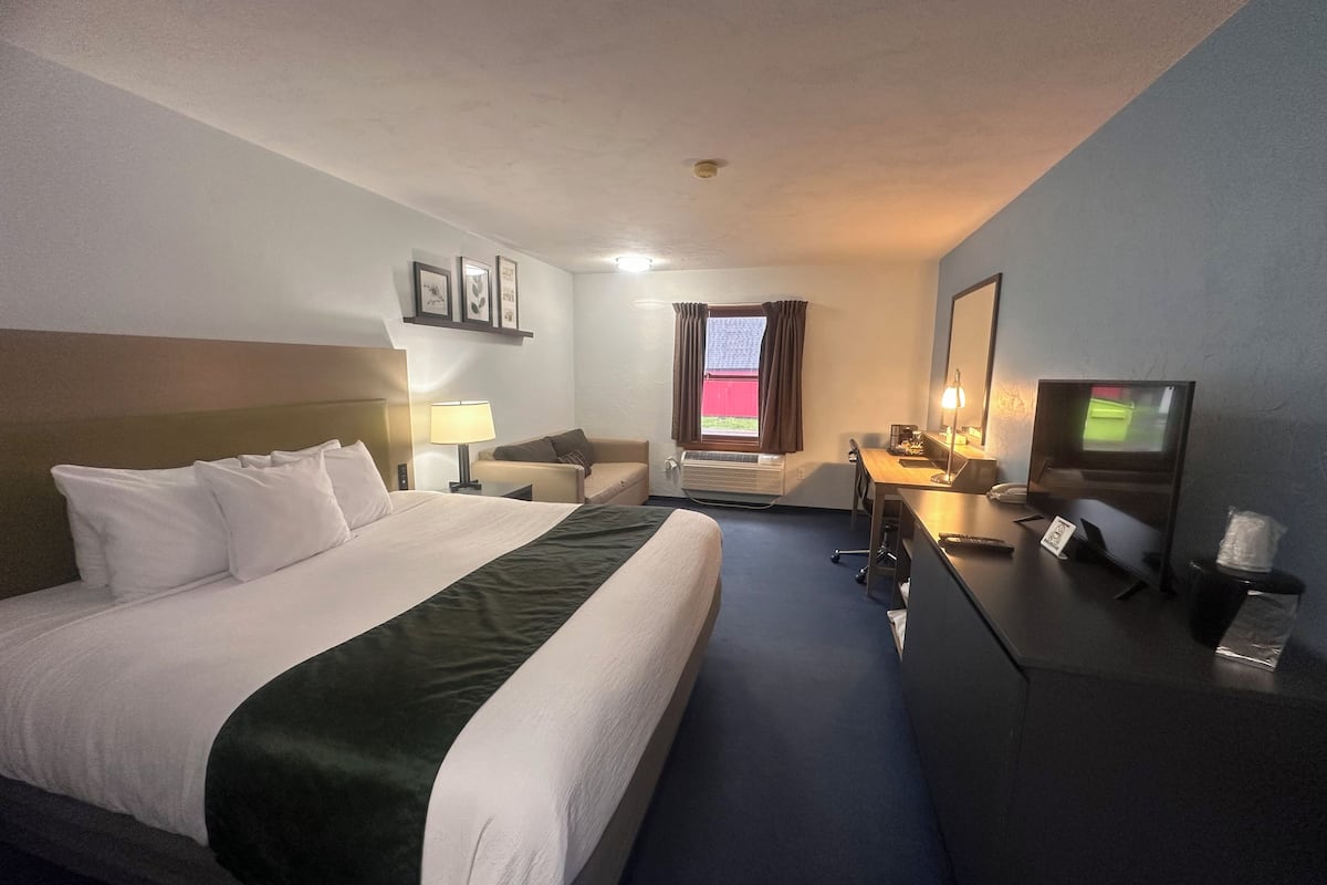 A hotel room with a large bed, a desk with a computer, a chair, a TV, and a window with curtains.