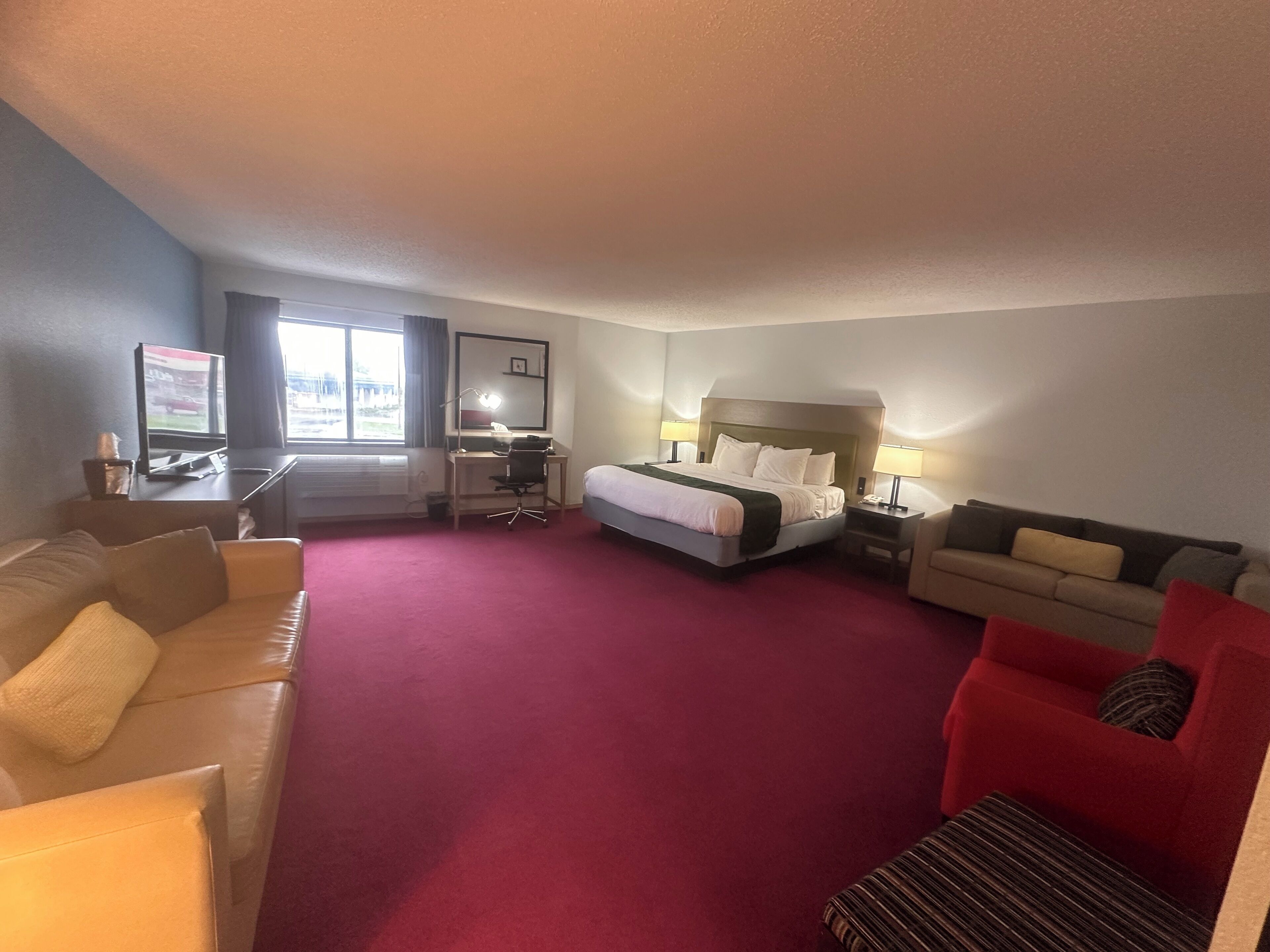 A hotel room with a bed, a desk, a chair, a sofa, and a TV.