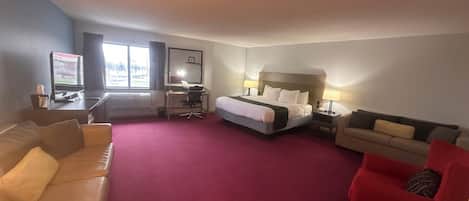 A hotel room with a bed, a desk, a chair, a sofa, and a TV.