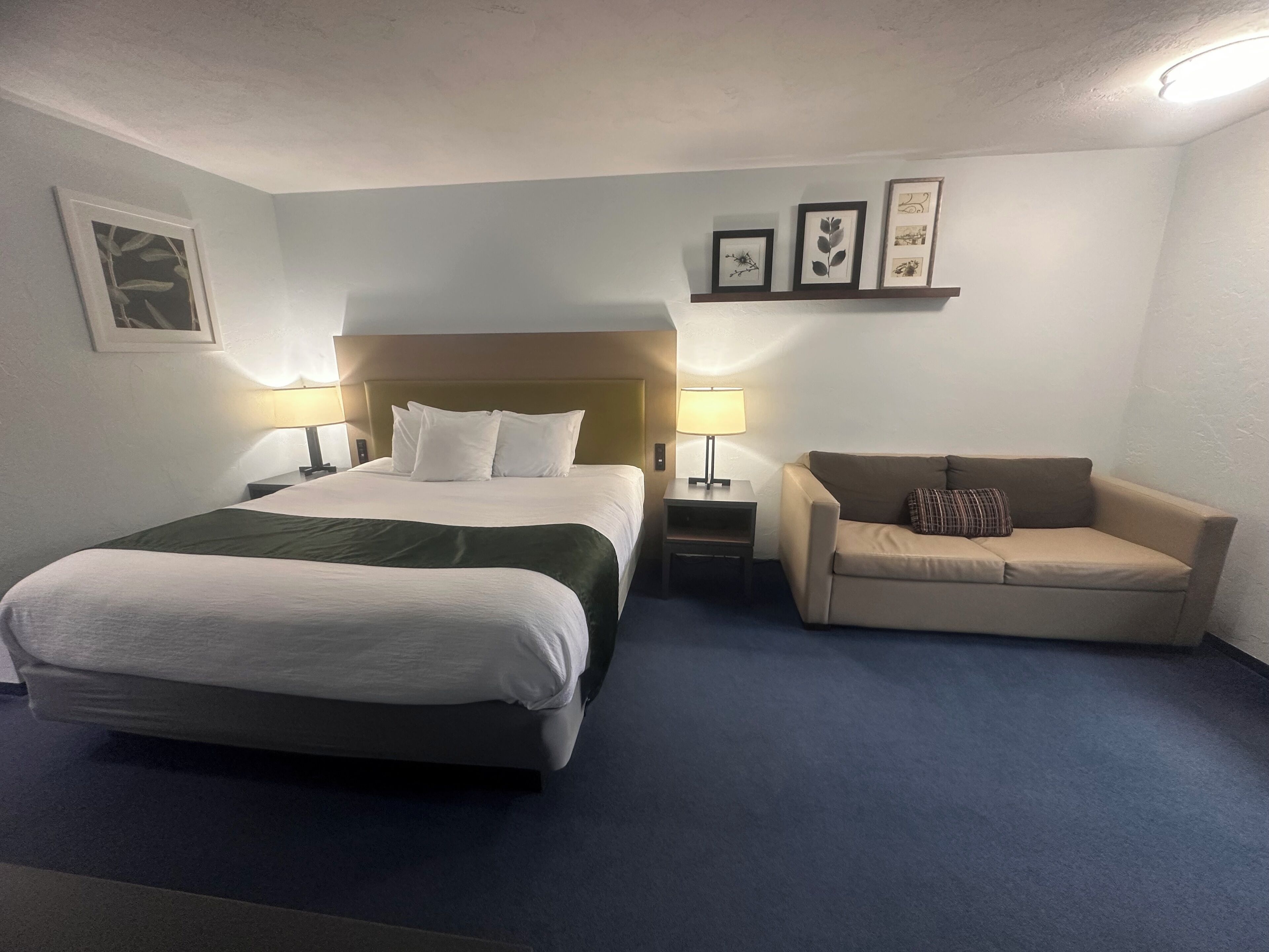 Ein Hotelzimmer mit einem großen Bett, einer Sitzecke, zwei Nachttischen mit Lampen und einer Wand mit gerahmten Bildern.
