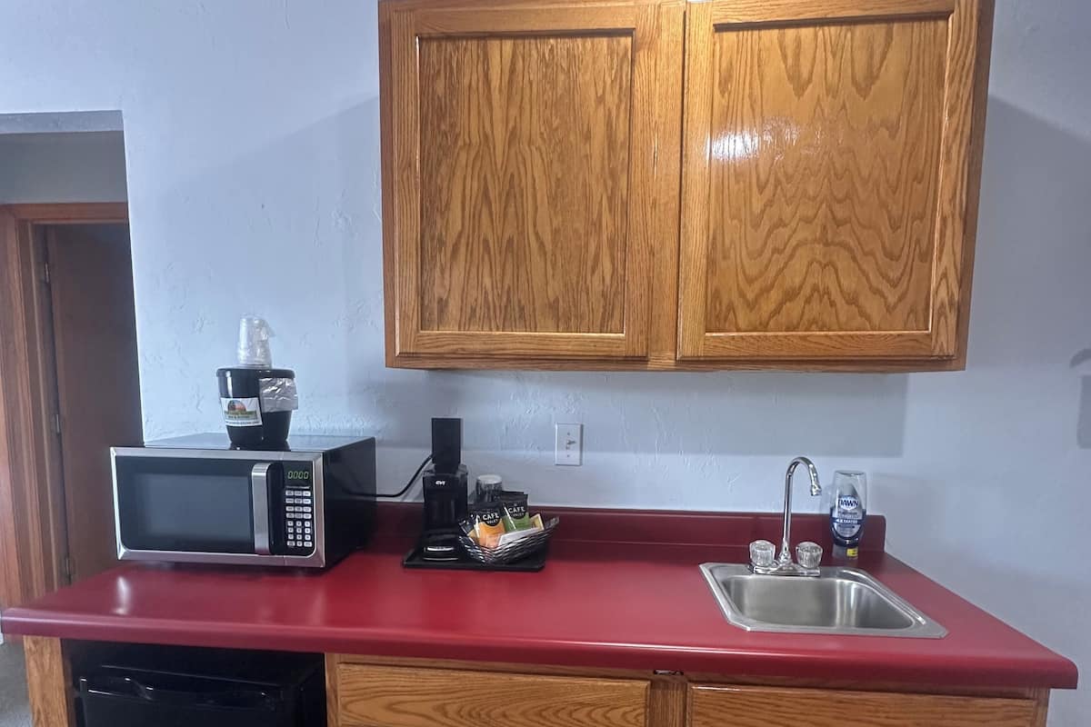 A compact kitchen with wooden cabinets, a red countertop, a microwave, a coffee maker, and a dishwasher.
