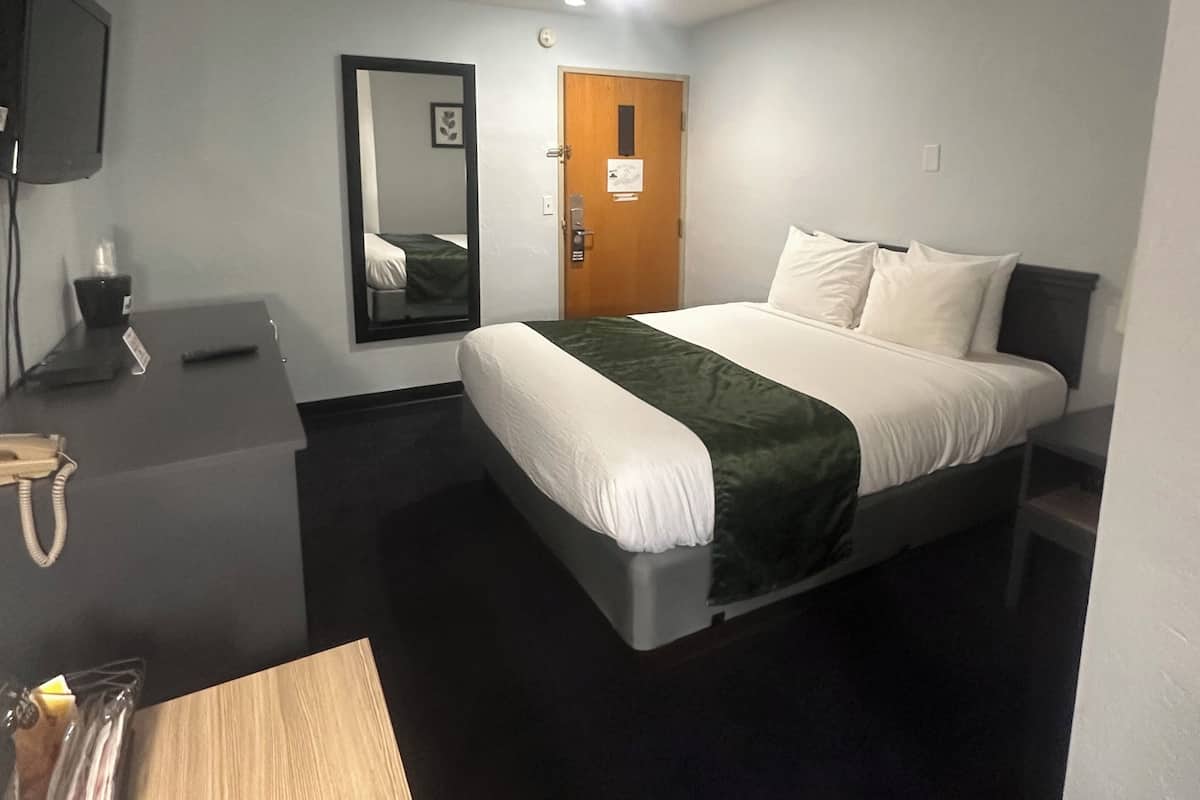 A hotel room with a bed, a desk, a chair, a TV, and a door.