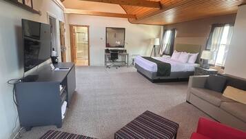 A cozy hotel room with a wooden ceiling, a bed, a desk with a chair, a TV, and a sofa.