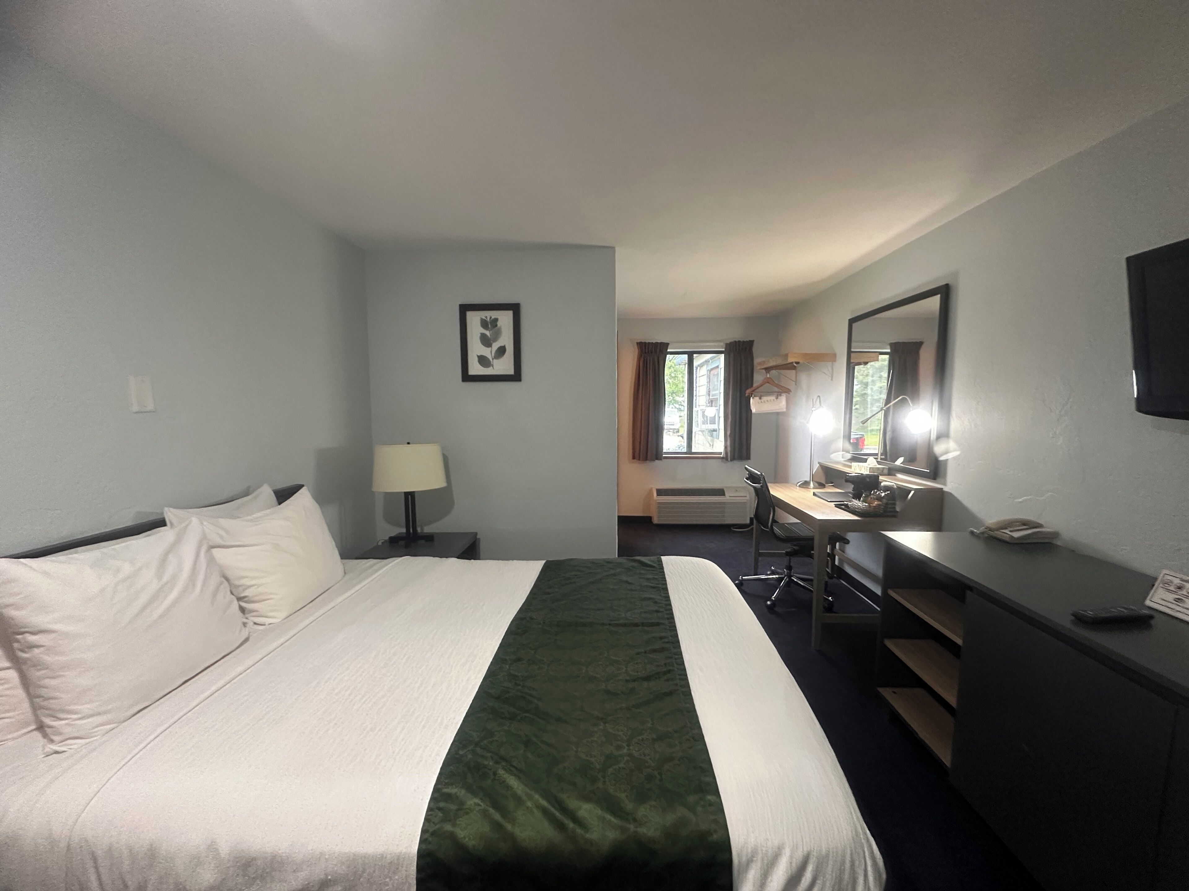 A hotel room with a bed, desk, chair, and a mirror.