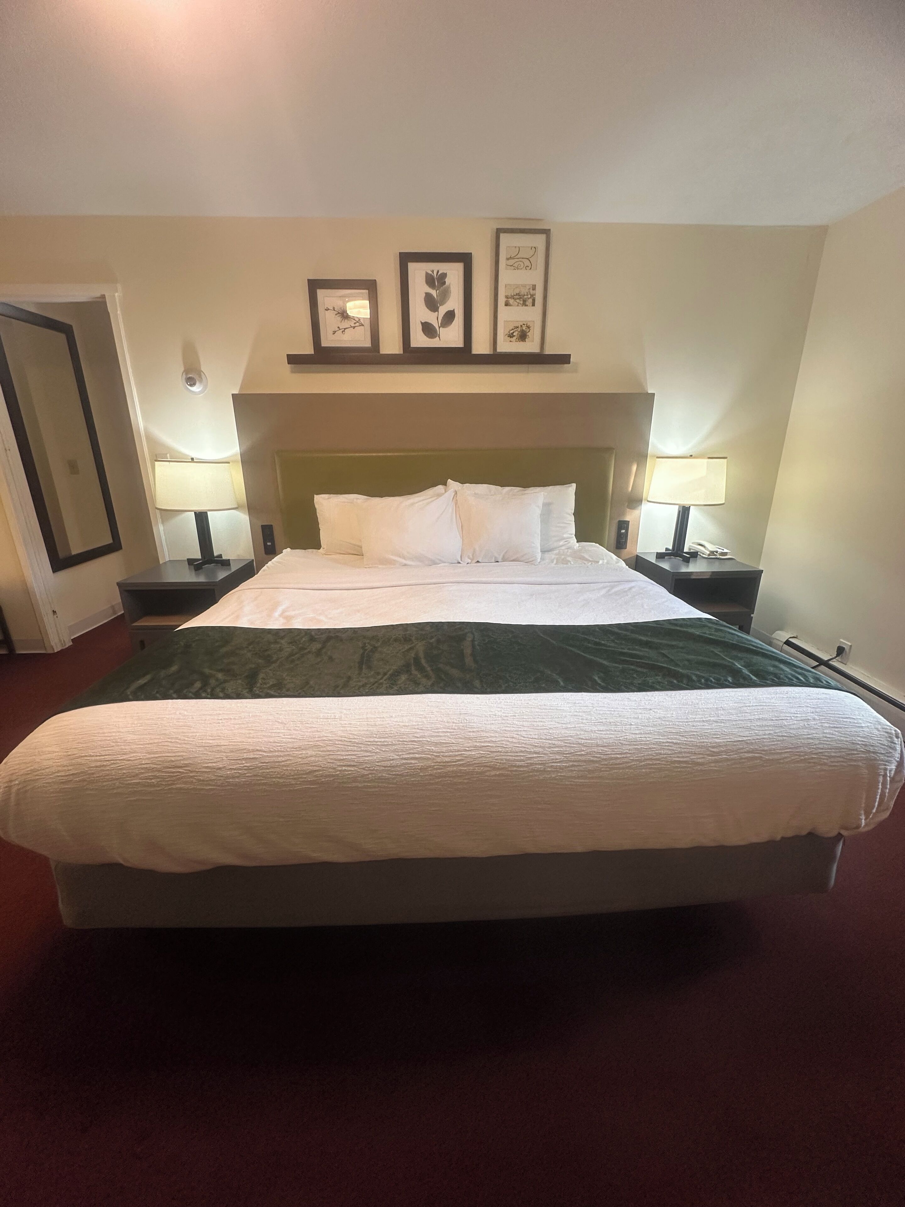 A hotel room with a large bed, two bedside tables with lamps, a headboard, and three framed pictures on the wall.