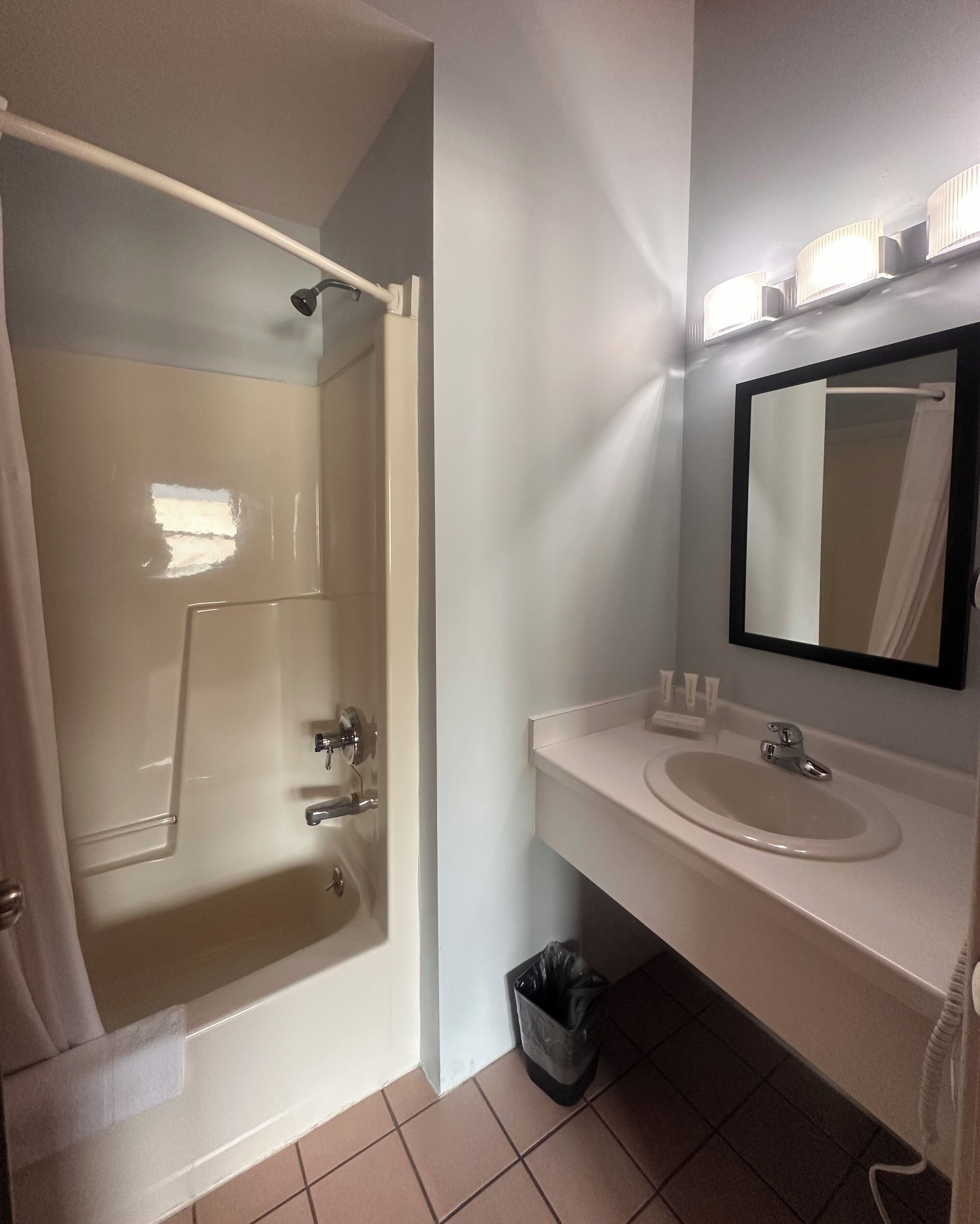 Un baño con bañera, lavabo, espejo y un cubo de basura.
