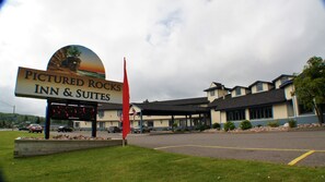 A hotel named 'Picture Rocks Inn & Suites' with a large sign, a parking lot, and a building with multiple windows and a covered area.