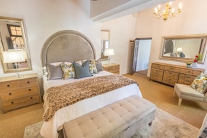A bedroom with a large bed, a chest of drawers, a vanity with a mirror, and a chandelier.