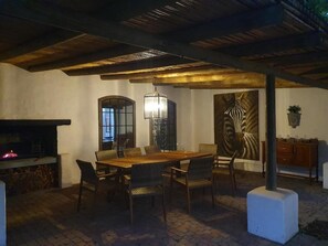 An indoor dining area with a brick floor, a wooden table, wicker chairs, a hanging light fixture, a fireplace, and a zebra mural.