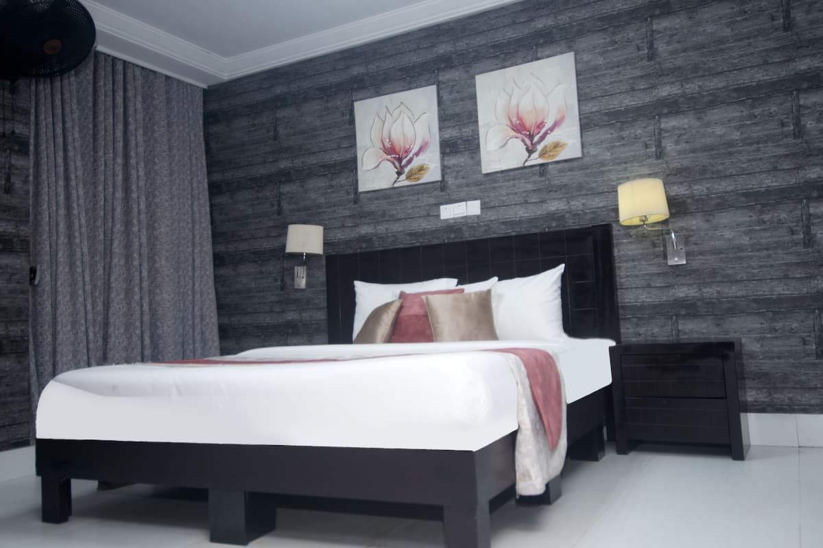 A modern bedroom with a large bed, dark headboard, two wall-mounted lamps, and two floral paintings.