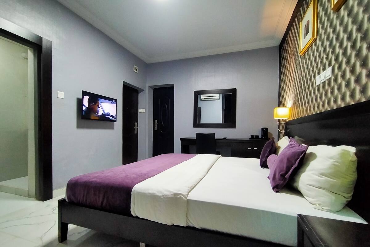 A hotel room with a bed, a TV mounted on the wall, a desk with a chair, and a mirror.