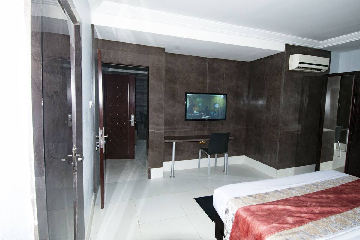 A modern hotel room with a large bed, a TV mounted on the wall, a desk, and a chair.