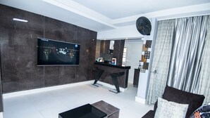 Ein modernes Wohnzimmer mit Flachbildfernseher, einer Couch, einem Couchtisch und einer Küche im Hintergrund.
