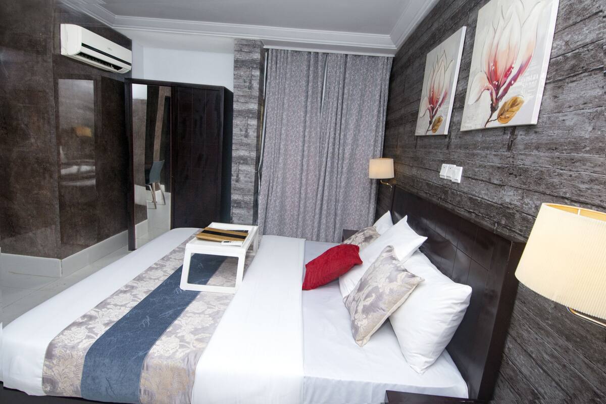 A hotel room with a bed, a bedside table, a lamp, a mirror, and artwork on the wall.
