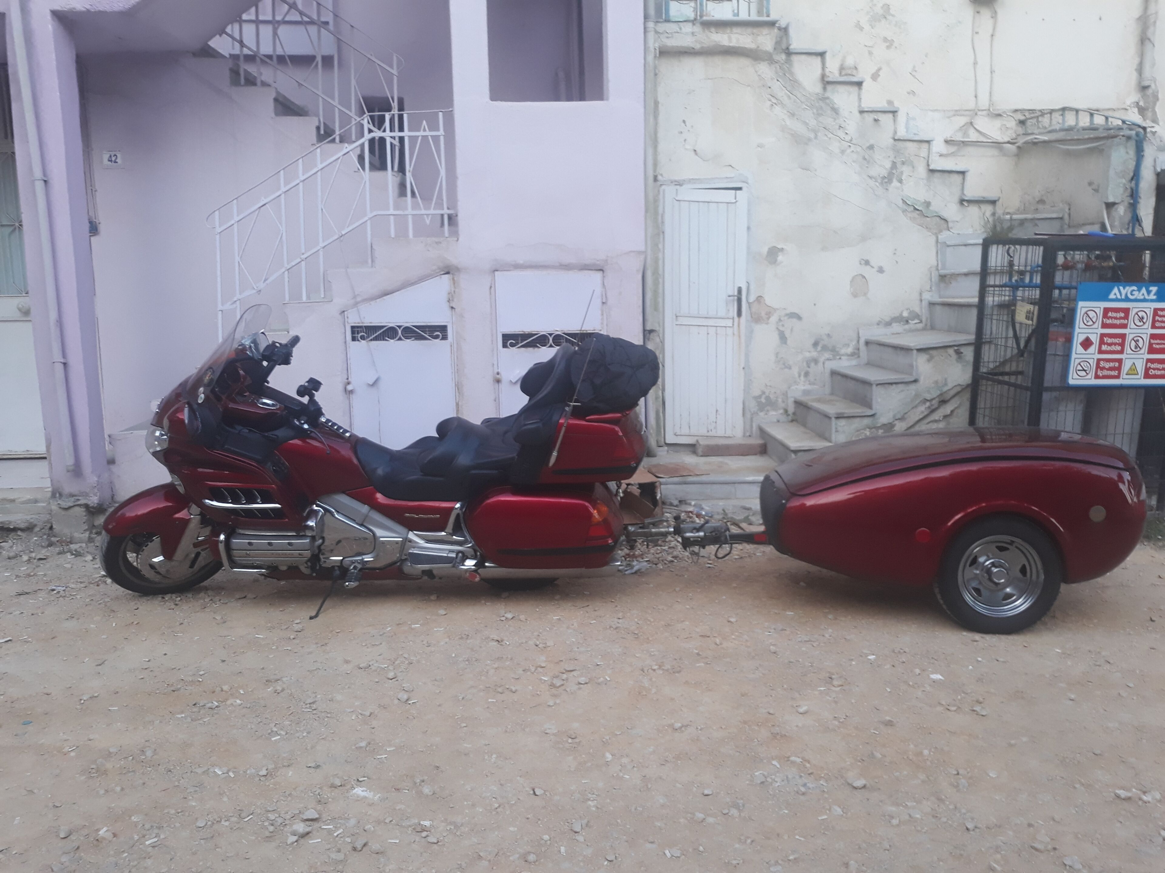 Ein rotes Motorrad mit Beiwagen vor einem Gebäude mit Treppe und einem Schild.