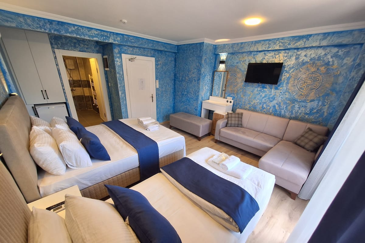A hotel room with two beds, a sofa, a TV, and a bathroom visible through an open door.