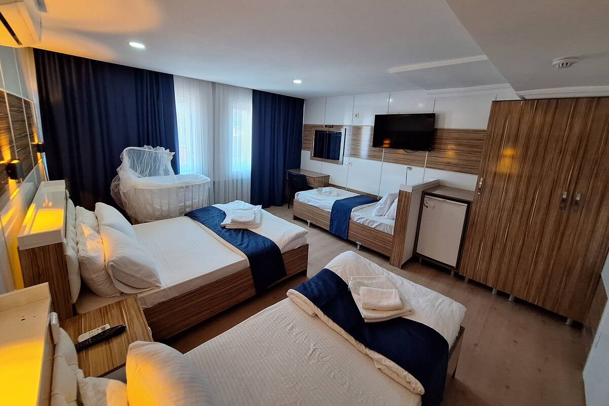 A hotel room with two beds, a desk, a TV, a crib, and a wardrobe.