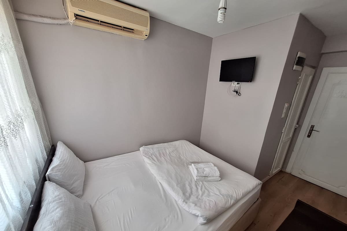 A single bed with white linens, a flat-screen TV mounted on the wall, and a door with a handle.