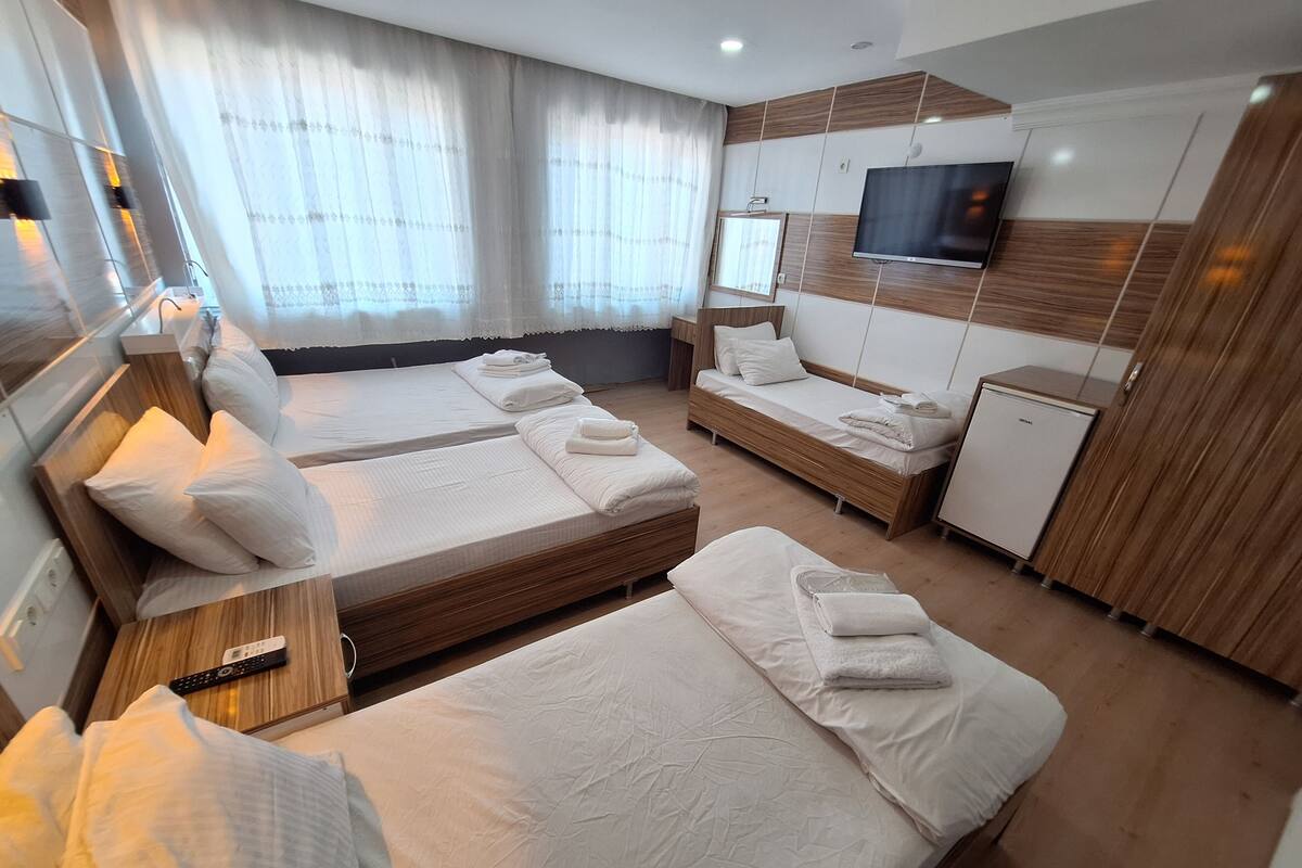 A hotel room with two beds, a TV, a mini-fridge, and a large window with curtains.