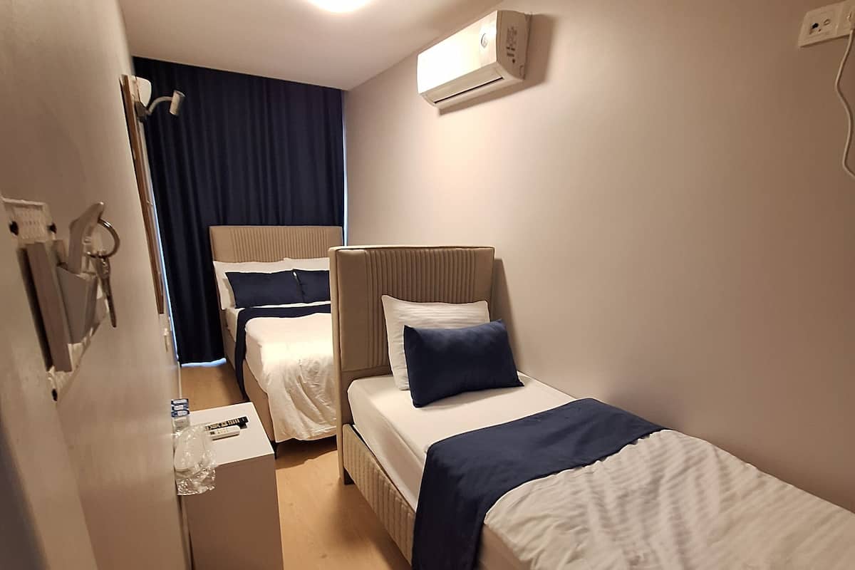 A hotel room with two beds, a bedside table, a small desk, and an air conditioning unit.