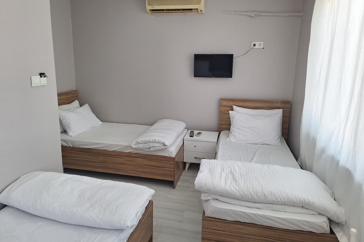 A hotel room with two beds, a TV, an air conditioner, and a bedside table.
