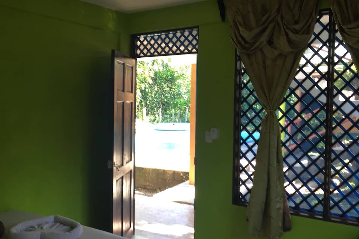 Ein Zimmer mit grünen Wänden, einem Bett, einem Fenster mit Vorhang und Blick auf einen Pool.
