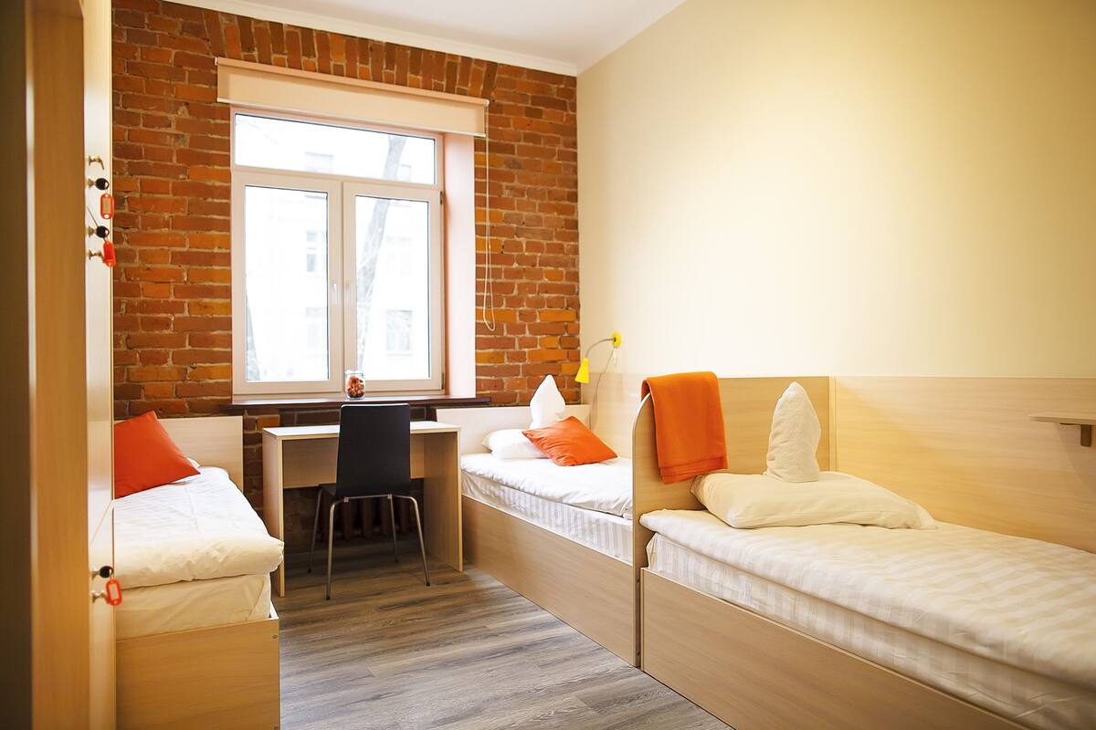 A compact room with a brick wall, a window, a desk, and two beds.