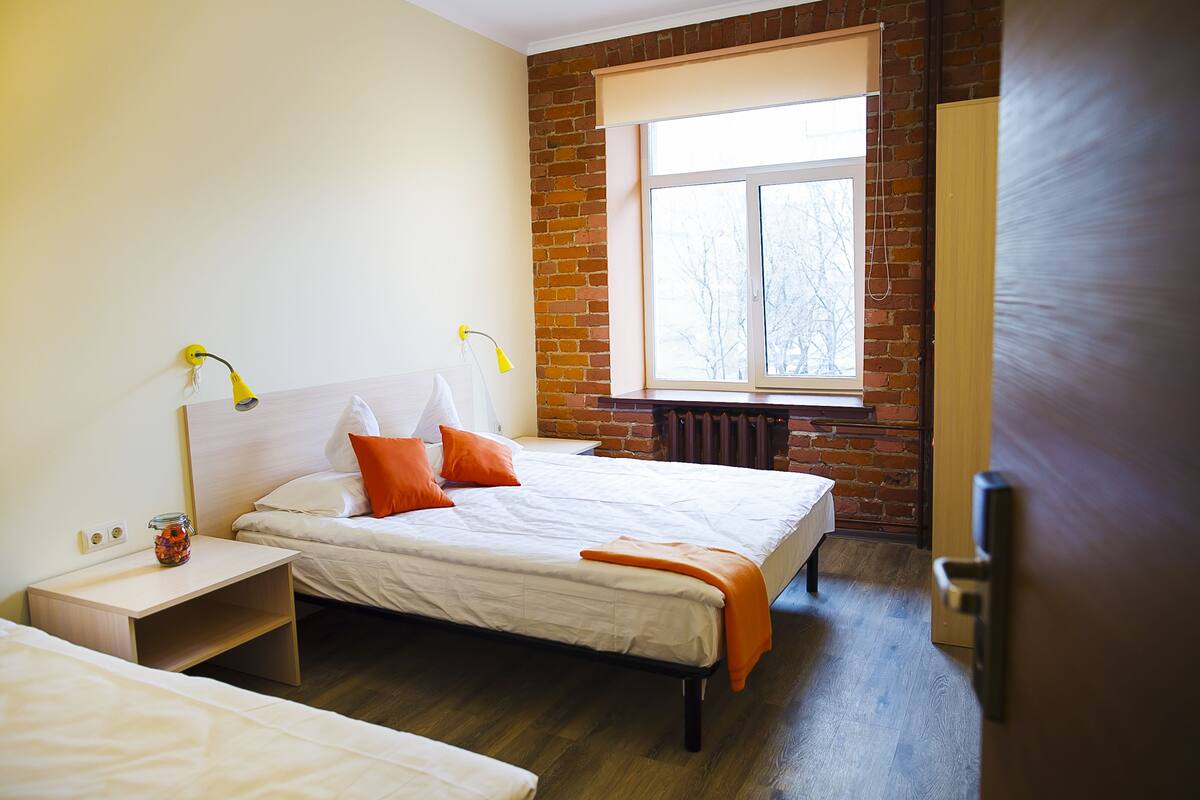 A bedroom with two beds, a brick wall, a window, and a radiator.