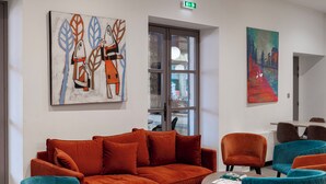 A modern lounge area with a red sofa, teal and orange chairs, and abstract art on the walls. -  Logis Hotel-Restaurant Saint Romain (Anse)