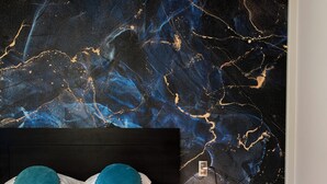 A modern bedroom with a large bed, two blue pillows, a dark headboard, a small round table with a lamp, and a blue chair. -  Logis Hotel-Restaurant Saint Romain (Anse)