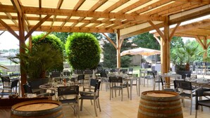 An outdoor dining area with wooden tables and chairs, surrounded by potted plants and a pergola structure. -  Logis Hotel-Restaurant Saint Romain (Anse)