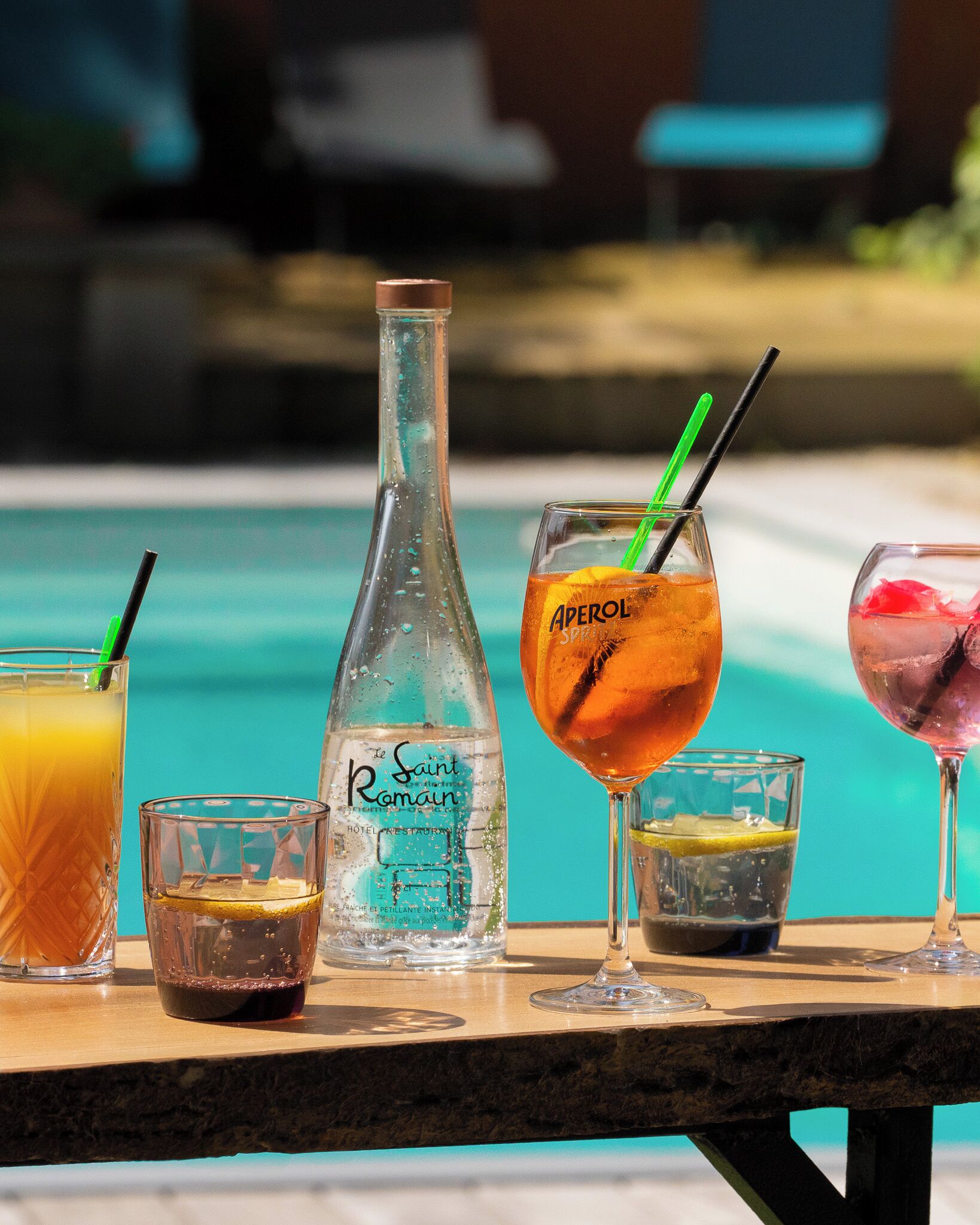 A variety of drinks on a table near a pool.