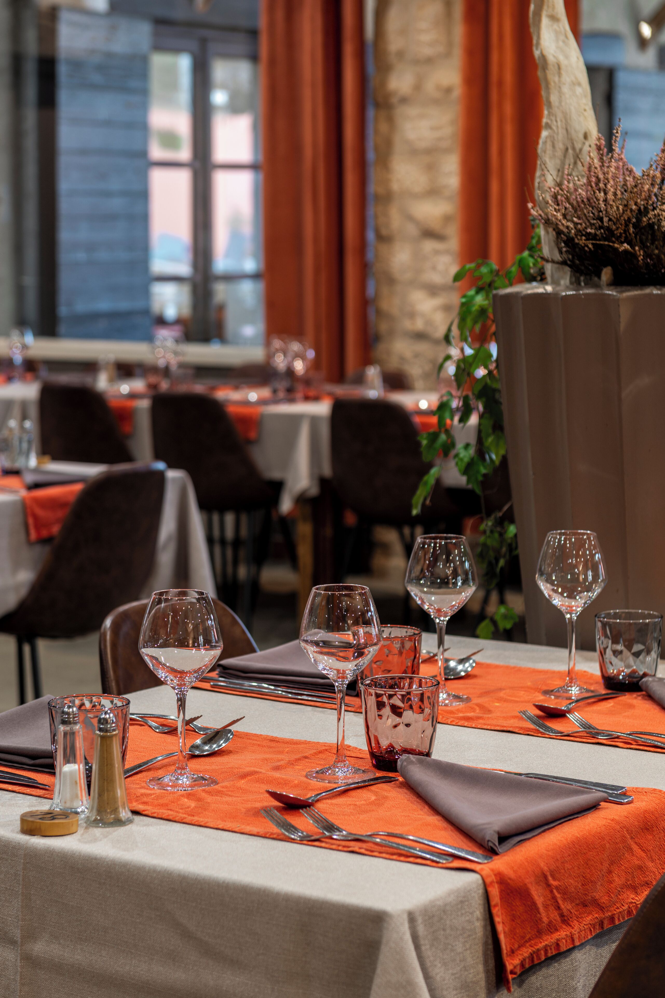 L’intérieur d’un restaurant, avec des tables dressées pour le service, agrémenté de nappes orange et de verres transparents.