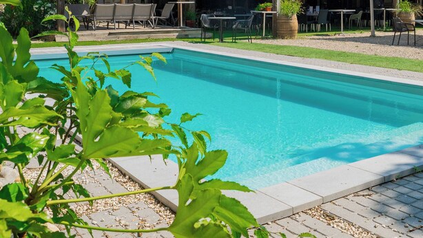 A poolside area with a covered patio, outdoor seating, and a stone building in the background. -  Logis Hotel-Restaurant Saint Romain (Anse)