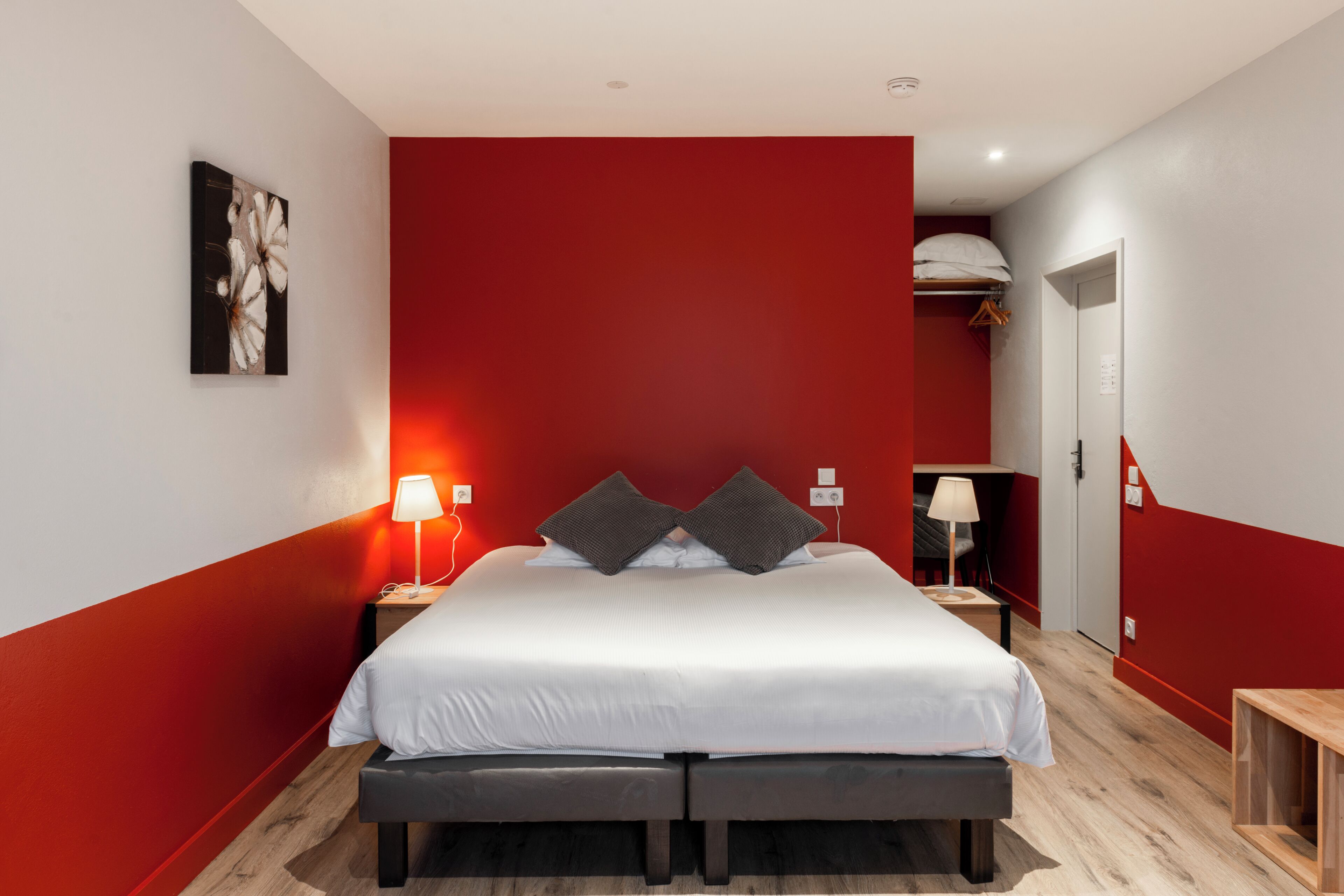 Une chambre moderne avec un grand lit, des murs d’un rouge vif et un plancher en bois.