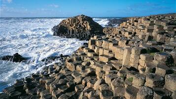 A rocky coastal area with large hexagonal stone structures and a prominent rock formation in the background.