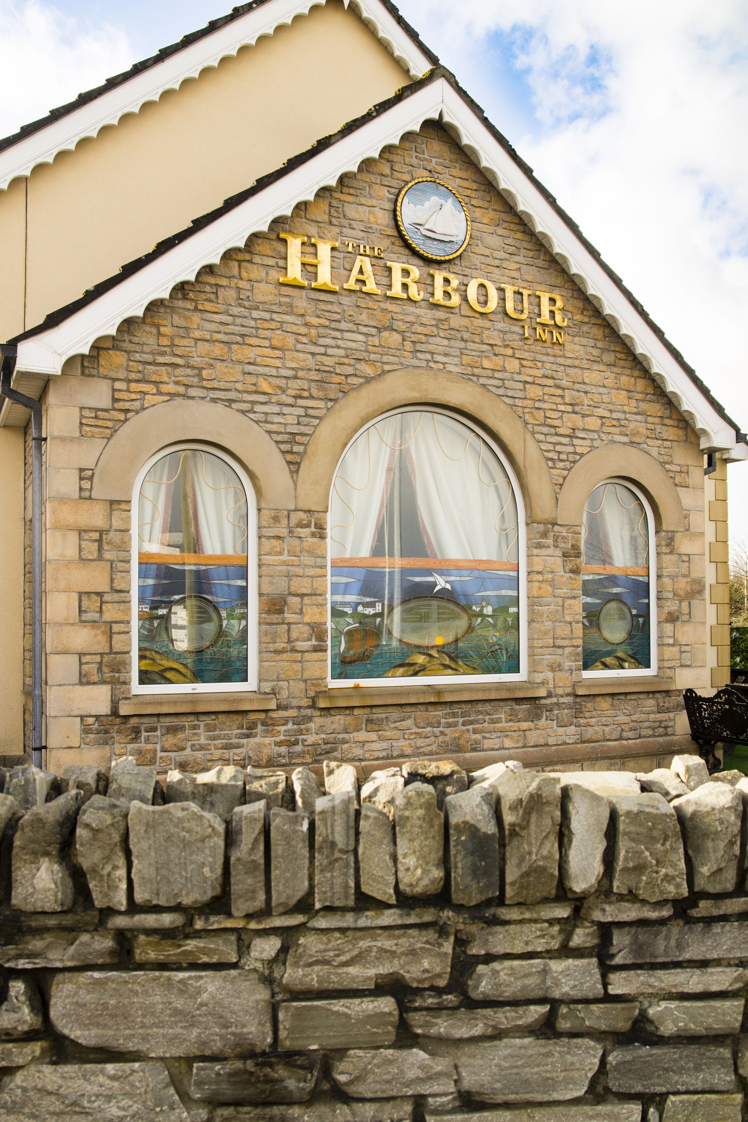 A stone building with the sign "The Harbour Inn" and three arched windows with curtains.