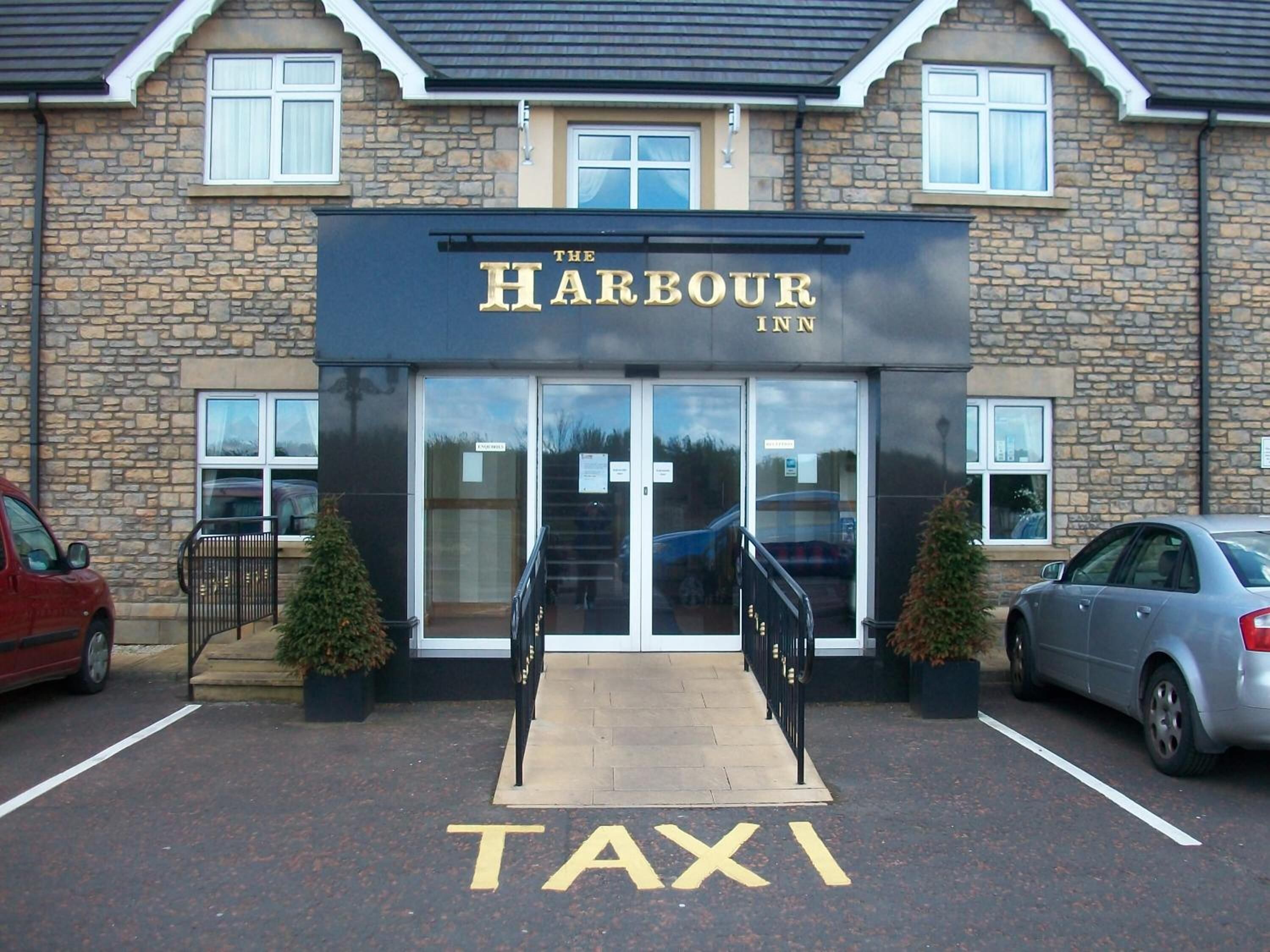 El Harbour Inn, con entrada despejada, señalización de parada de taxis y un estacionamiento con automóviles.
