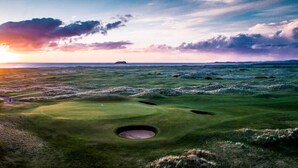 A golf course with a single hole, surrounded by grassy terrain and a sunset in the background. - The Harbour Inn (Buncrana)