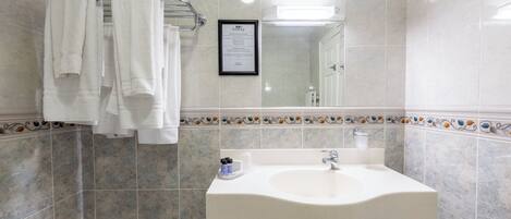 A bathroom with a white sink, a towel rack with multiple towels, a framed sign on the wall, and decorative tile border.