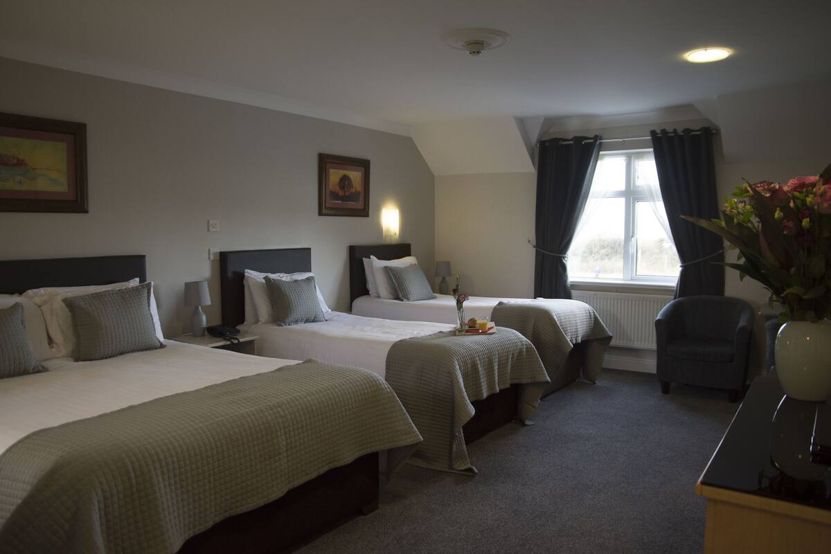 Habitación de hotel con dos camas, un escritorio, una silla y una ventana con cortinas.