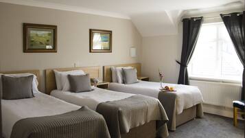 A hotel room with two single beds, a small table with a plate of fruit, and a window with curtains.