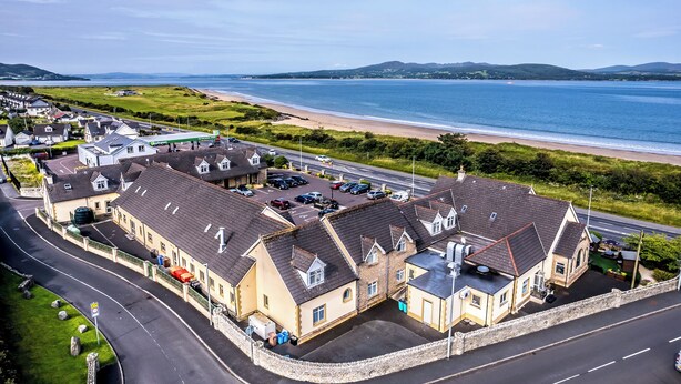 A coastal residential area with houses along a road, a beach, and a clear view of the sea. - The Harbour Inn (Buncrana)