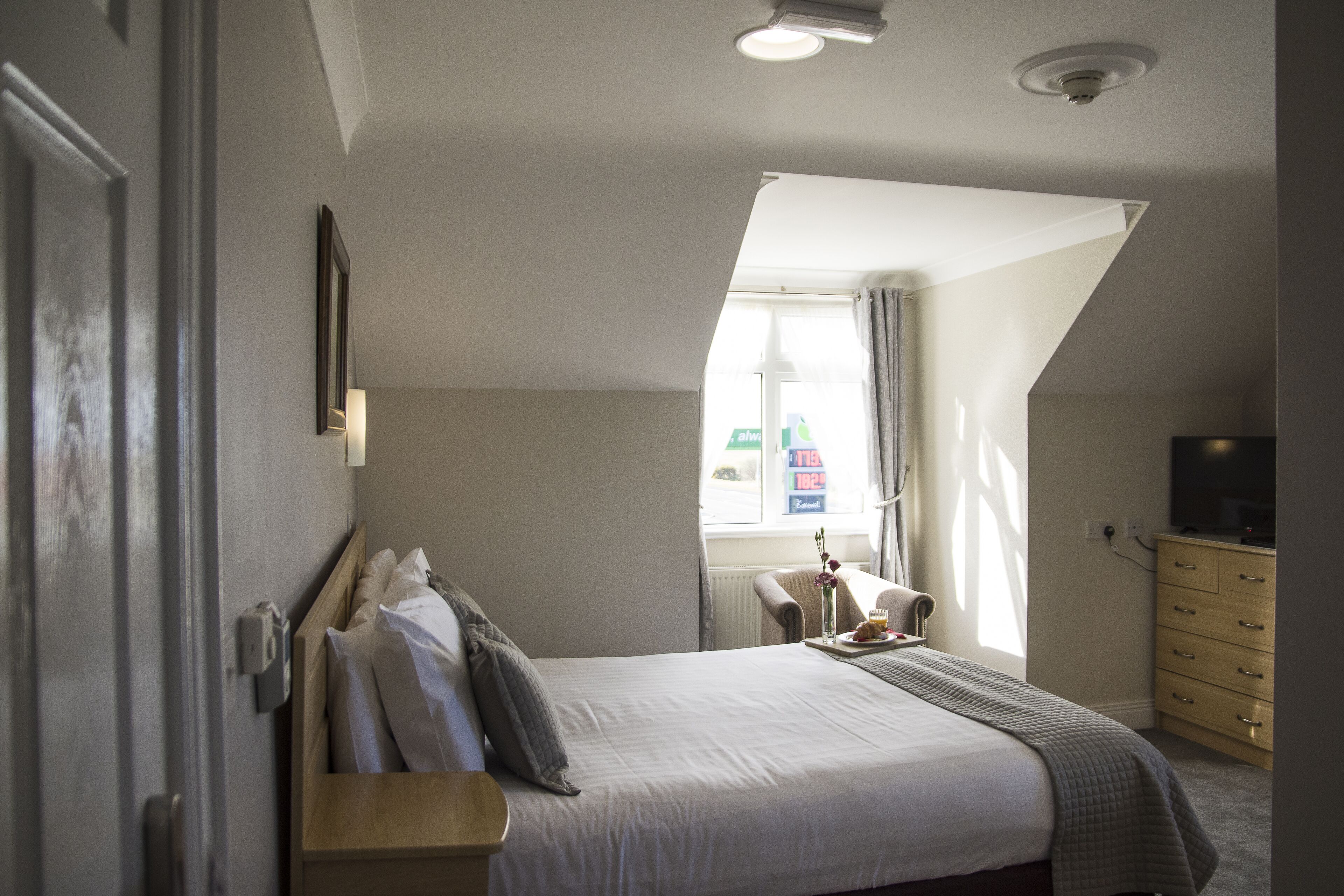 A bedroom with a bed, a dresser, a nightstand, and a window with curtains.
