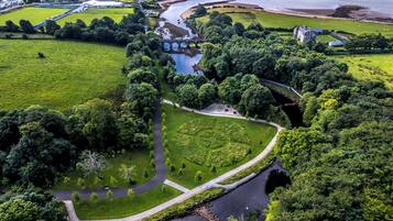 An aerial view of a park with a river, a bridge, and a historic building.