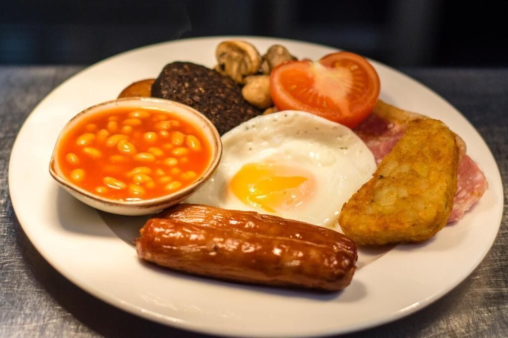 A plate with a fried egg, sausage, baked beans, mushrooms, tomato, and hash browns.