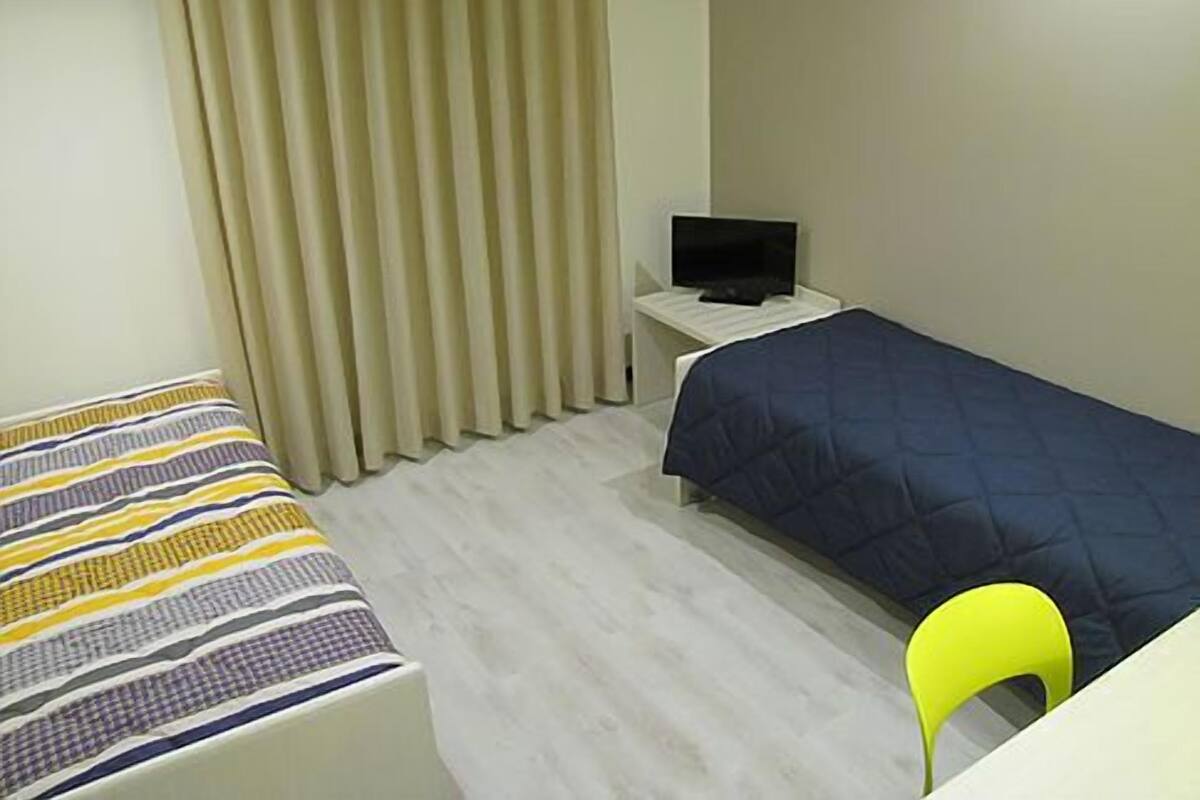 Una habitación pequeña y sencilla con una cama, un escritorio con ordenador y una silla.