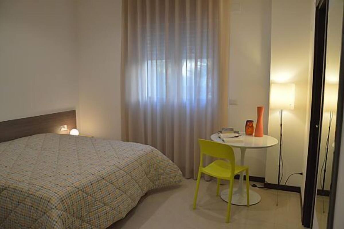 Una habitación de hotel con cama, una silla, una mesita y una lámpara.